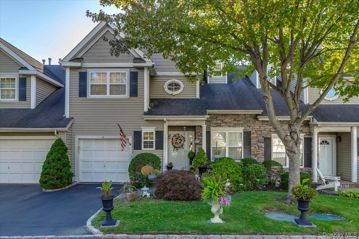 View of front of property with stone siding, asphalt driveway, a front lawn, a shingled roof, and a garage
