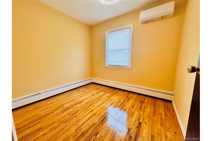 Unfurnished room with light wood-type flooring, baseboard heating, and a wall unit AC