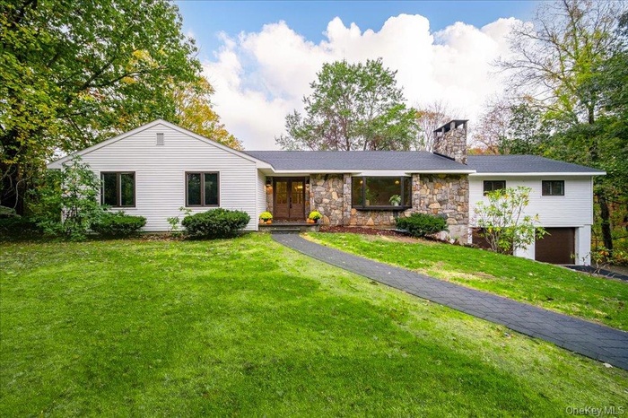 Ranch-style house featuring a chimney, a front lawn, a garage, and stone siding