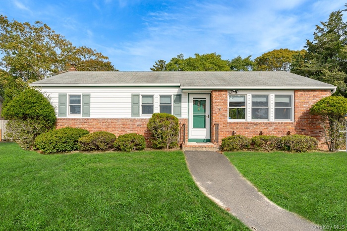 View of front of home with a front yard, brick siding, and roof with shingles