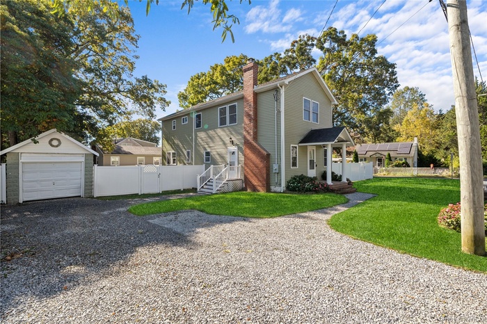 View of front of house featuring a chimney, an outdoor structure, driveway, a detached garage, and a gate