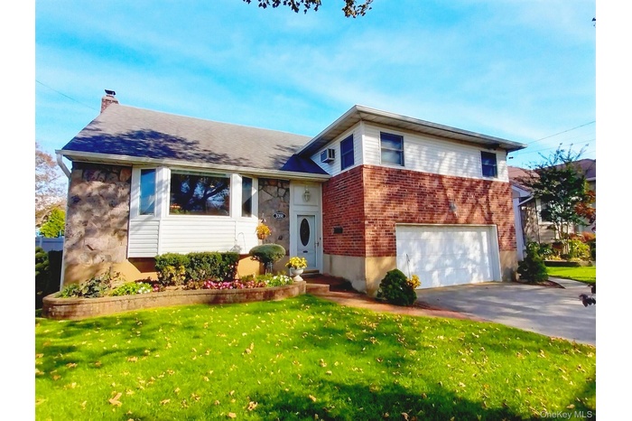 Tri-level home with a front lawn, a chimney, driveway, and an attached garage