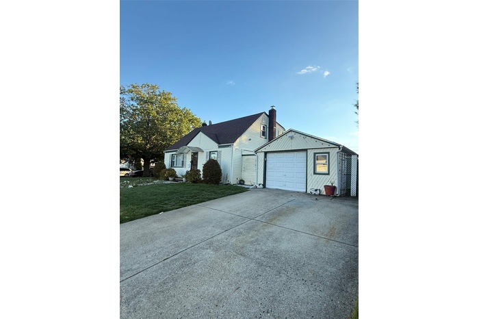 Ranch-style home with concrete driveway, a garage, a chimney, and a front lawn