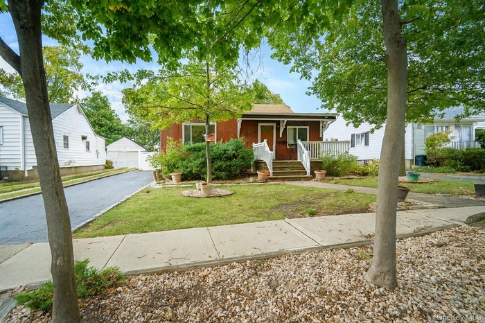 Bungalow-style house featuring covered porch, an outbuilding, a front lawn, and a detached garage