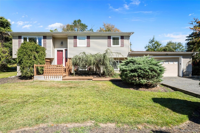 Split foyer home with a garage, a front lawn, a wooden deck, and asphalt driveway