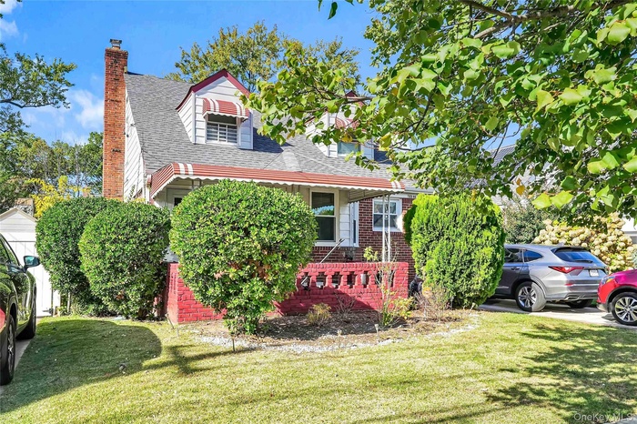 Cape cod-style house featuring a shingled roof, brick siding, a front lawn, and a chimney