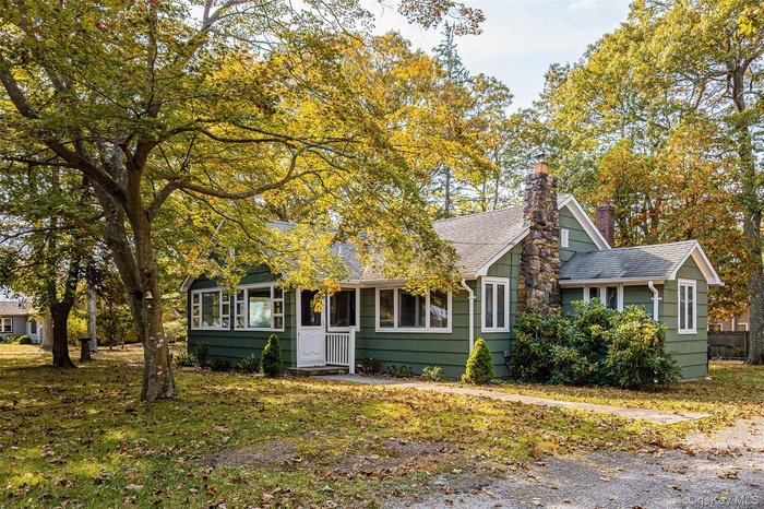 View of front facade featuring roof with shingles, a chimney, and a front lawn