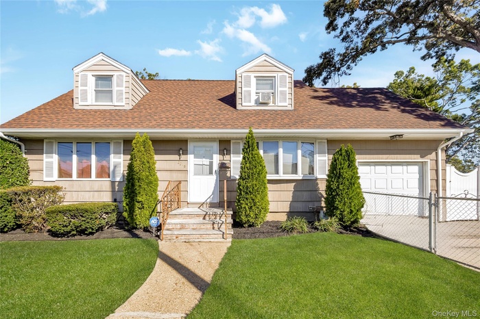 Cape cod house featuring a shingled roof, an attached garage, driveway, and a gate