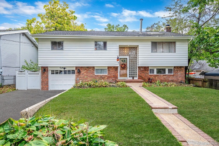 Raised ranch with brick siding, a chimney, a garage, and driveway