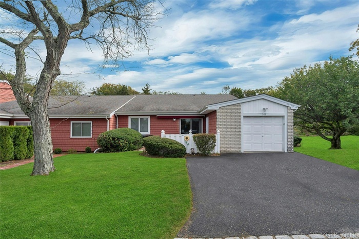 Ranch-style home featuring driveway, a front yard, a shingled roof, and a garage