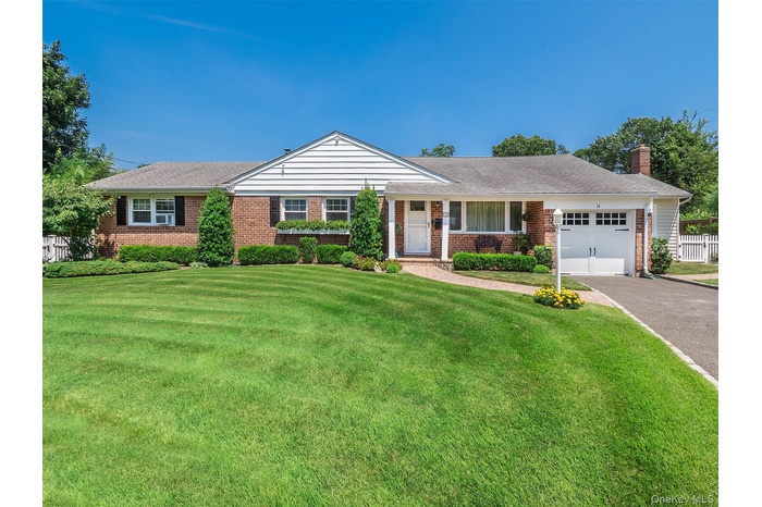 Ranch-style house featuring covered porch, a chimney, a garage, asphalt driveway, and brick siding