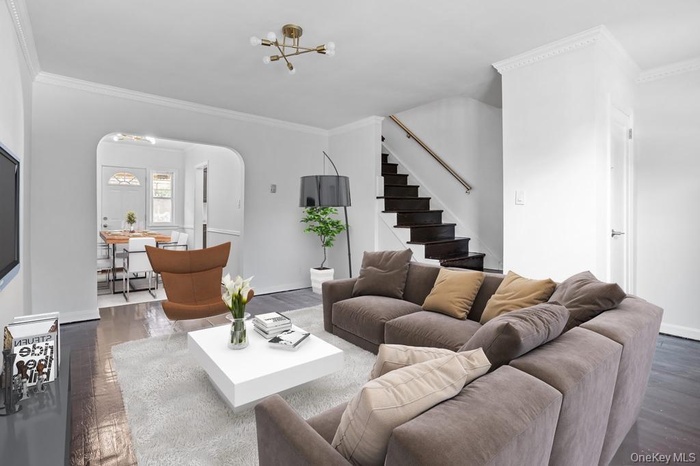 Living area with arched walkways, a chandelier, stairway, wood finished floors, and ornamental molding