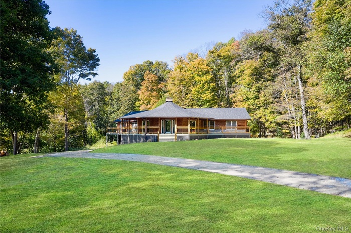 View of front facade featuring a porch, a front yard, a chimney, and a wooded view