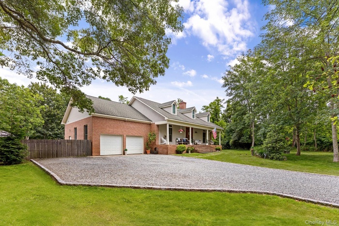Cape cod-style house featuring covered porch, brick siding, roof with shingles, driveway, and an attached garage