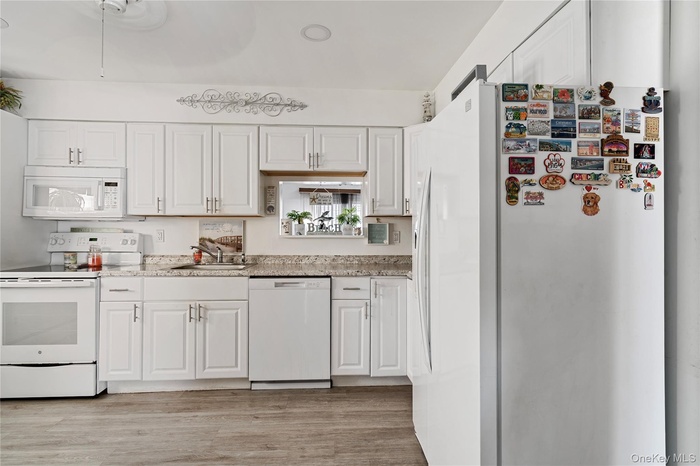 Kitchen featuring white appliances, white cabinets, light wood-type flooring, and light stone counters