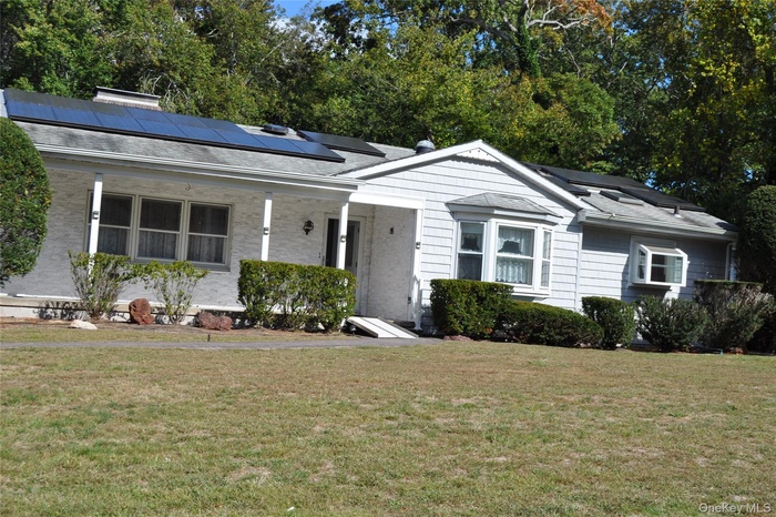 View of front of home with a front lawn, roof mounted solar panels, covered porch, a shingled roof, and a chimney