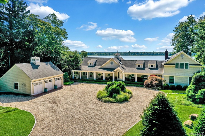 Shingle-style home with a chimney, covered porch, a garage, an outdoor structure, and driveway