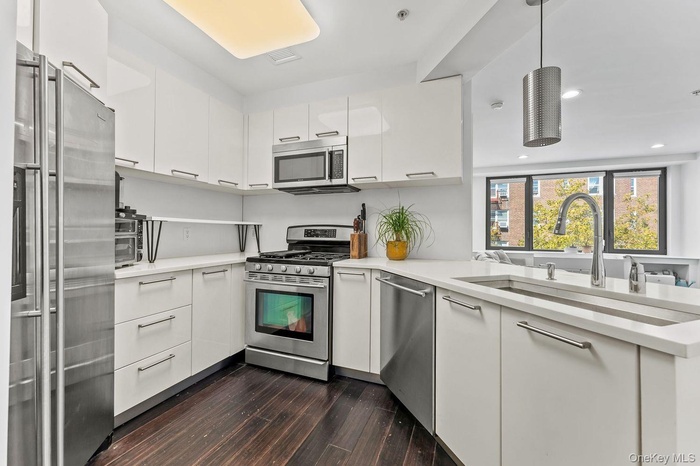 Kitchen featuring white cabinets, appliances with stainless steel finishes, modern cabinets, pendant lighting, and dark wood-style floors