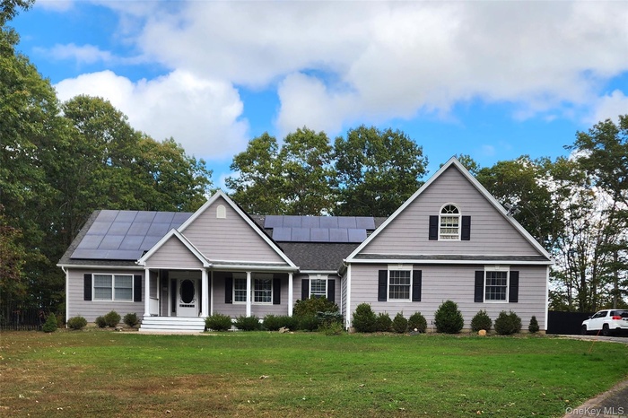 View of front of property with covered porch, roof mounted solar panels, and a front yard
