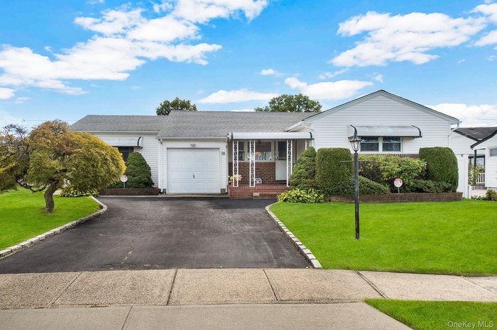 Ranch-style home featuring a front yard, covered porch, driveway, roof with shingles, and brick siding