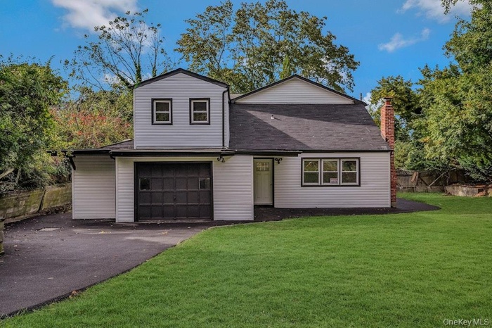 View of front of home with asphalt driveway, a chimney, an attached garage, and a shingled roof