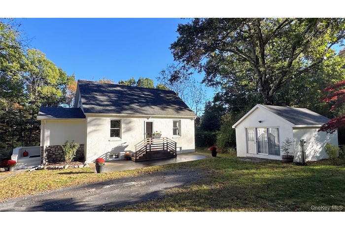 View of front of home featuring roof with shingles, an outbuilding, a front lawn, and stucco siding