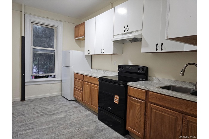 Kitchen with black electric range oven, light countertops, freestanding refrigerator, light wood-type flooring, and under cabinet range hood