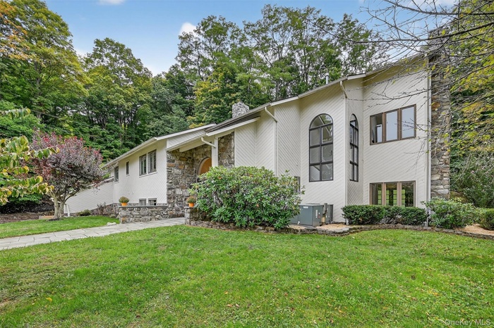 View of front facade with a chimney, stone siding, a front yard, and view of wooded area