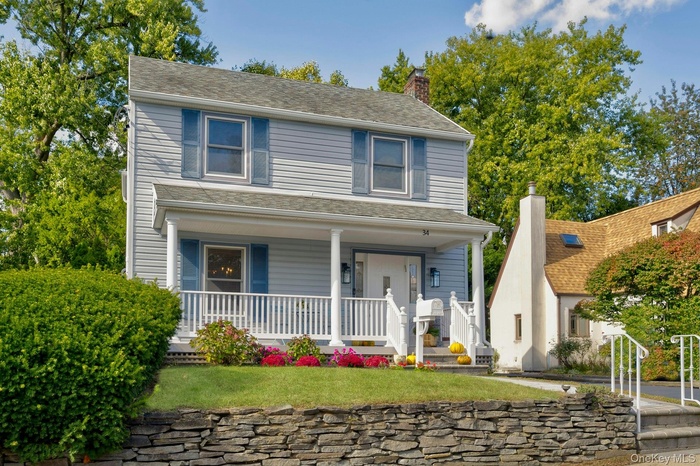 View of front facade featuring covered porch, a chimney, a front lawn, and roof with shingles
