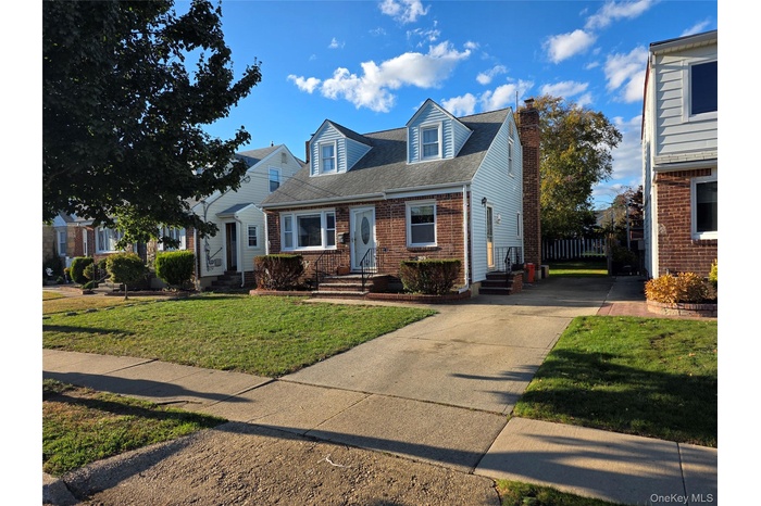 Cape cod house featuring roof with shingles, a front lawn, brick siding, a chimney, and concrete driveway