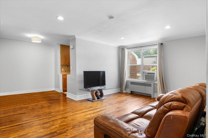 Living room featuring crown molding, radiator heating unit, wood finished floors, and recessed lighting