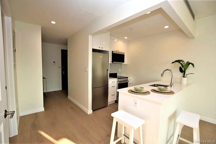 Kitchen with white cabinets, appliances with stainless steel finishes, light wood-style flooring, a breakfast bar area, and recessed lighting
