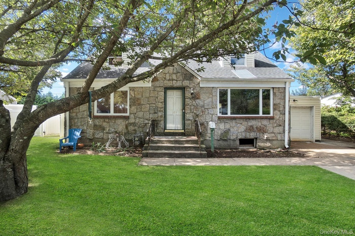 View of front of property featuring stone siding, a front yard, roof with shingles, and driveway