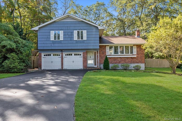 Split level home with brick siding, asphalt driveway, a garage, and a chimney