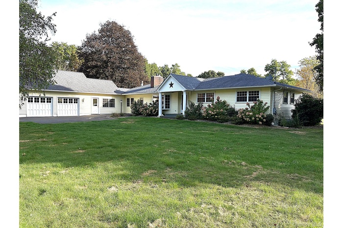 Ranch-style house featuring a front lawn, an attached garage, a chimney, and driveway