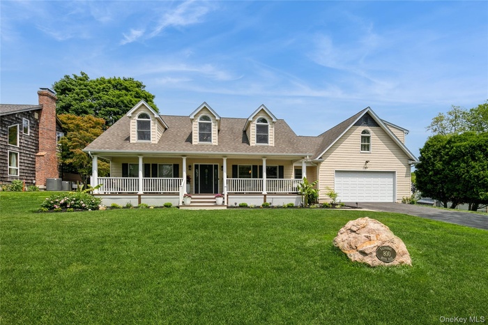 New england style home featuring driveway, a porch, a garage, a shingled roof, and a front lawn