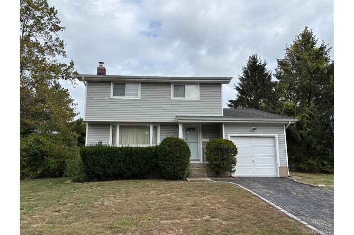 Traditional home featuring a garage, asphalt driveway, a front lawn, and a chimney