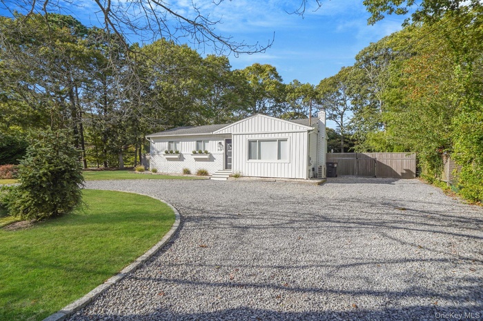 View of front of home with board and batten siding, driveway, view of wooded area, a chimney, and a shingled roof