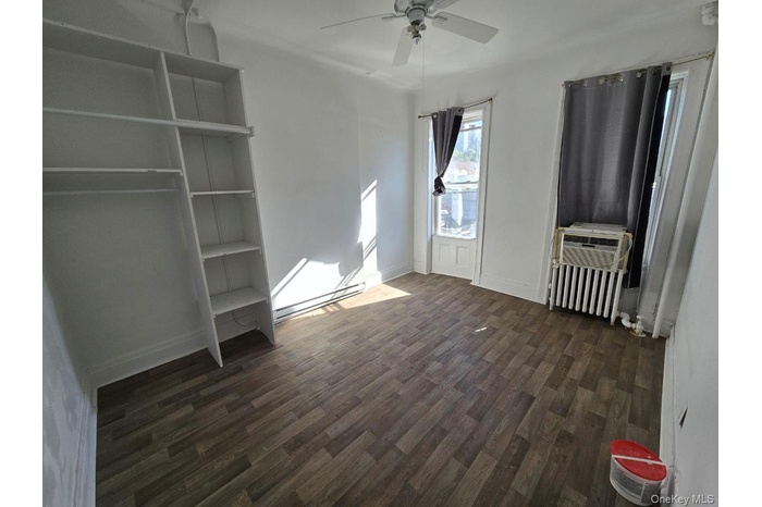 Unfurnished bedroom featuring dark wood-type flooring, radiator heating unit, a ceiling fan, a baseboard radiator, and cooling unit
