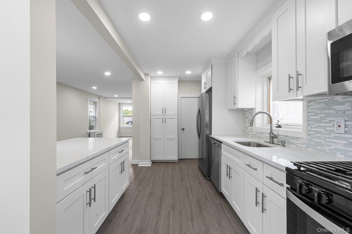Kitchen featuring white cabinetry, dark wood-style floors, light stone countertops, recessed lighting, and healthy amount of natural light