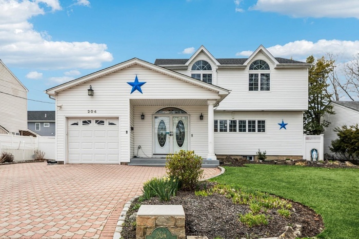View of front of house featuring an attached garage, fence, a front lawn, and decorative driveway