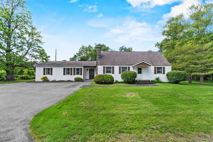 Ranch-style house featuring a front lawn, a chimney, and asphalt driveway
