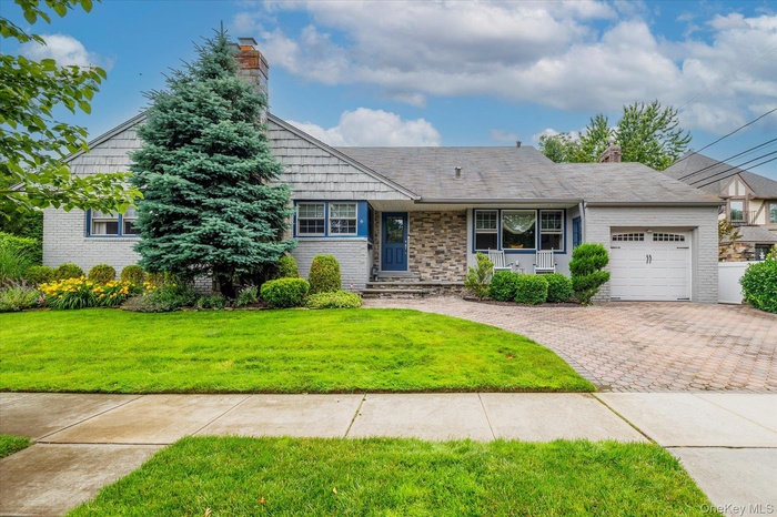 View of front of property featuring a chimney, an attached garage, decorative driveway, and a front lawn