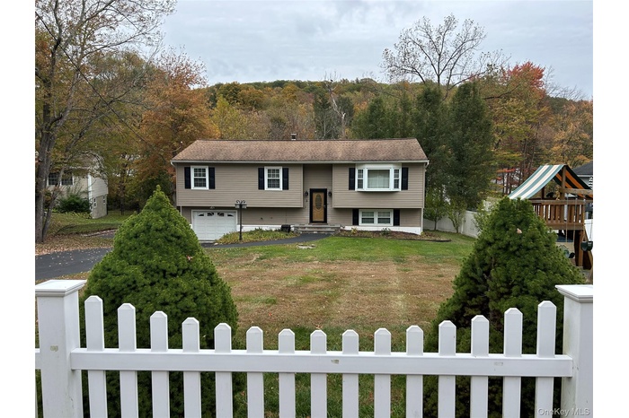 Raise Ranch home featuring a fenced front yard, a garage, driveway, and a playground