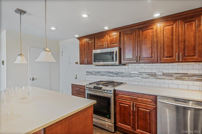 Kitchen featuring stainless steel appliances, hanging light fixtures, recessed lighting, tasteful backsplash, and light stone countertops
