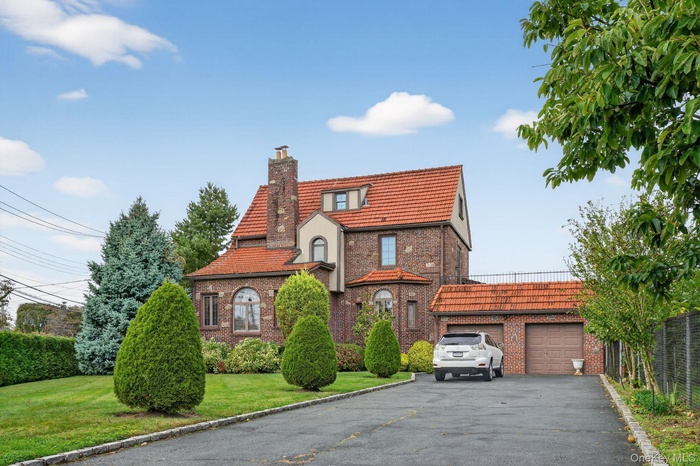 Tudor house featuring brick siding, a chimney, a garage, and a front lawn