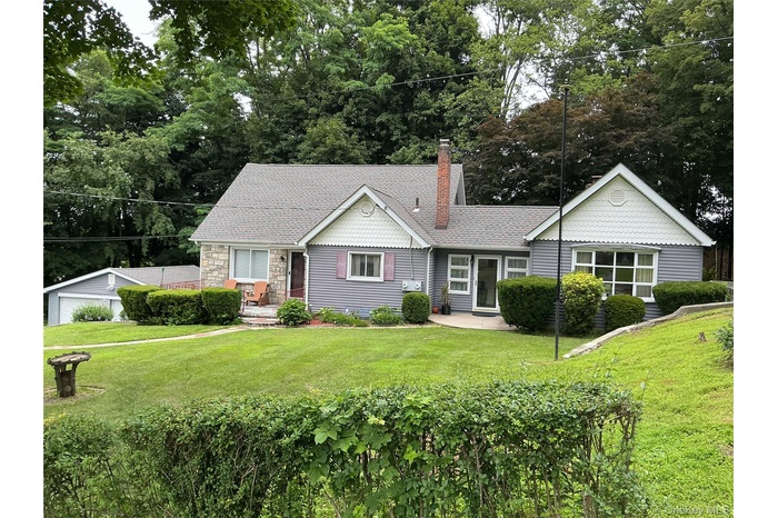 View of front of home featuring a front lawn, a chimney, a shingled roof, and stone siding