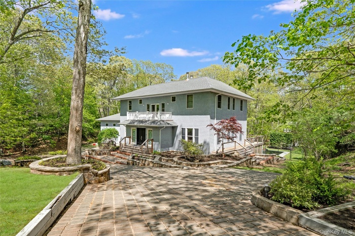 Back of house featuring a shingled roof, a chimney, view of wooded area, and a lawn
