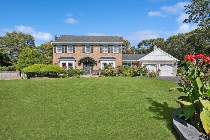 Colonial house with a front lawn, brick siding, driveway, and an attached garage