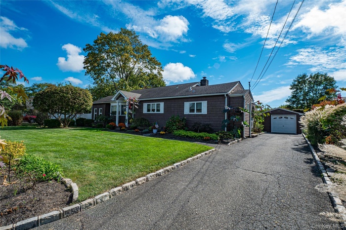 Ranch-style house with a front lawn, a chimney, an outdoor structure, a detached garage, and driveway